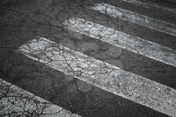 Pedestrian crossing marking on old damaged asphalt road