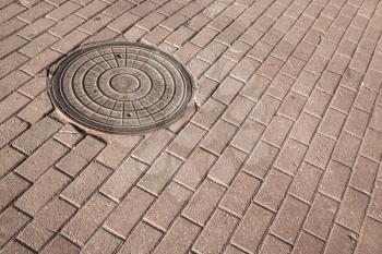 Round steel sewer manhole on the cobblestone pavement