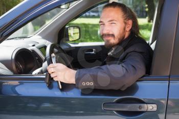 Bearded Asian man with keys as a driver of modern Japanese suv, outdoor portrait in open car window