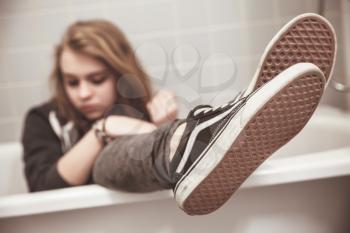 Teenage girl in black sporty sneakers sits in white bath. Closeup photo with selective focus on shoes, tonal filter correction, vintage stylized