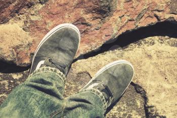 Male feet in canvas shoes and jeans standing on rough rocky ground, vintage warm tonal correction photo filter effect, old style effect