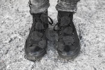 Teenager feet in black gumshoes standing on rough concrete floor
