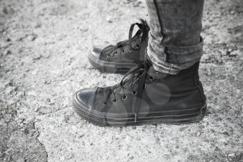 Teenager feet in black gumshoes and jeans standing on gray rough concrete floor