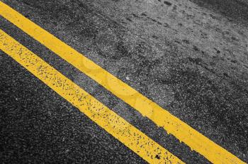 Yellow double dividing line over black highway asphalt, closeup photo with selective focus