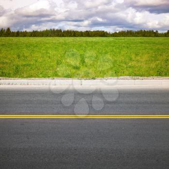 Empty highway roadside with yellow double dividing lines. Green summer grass and forest on a background