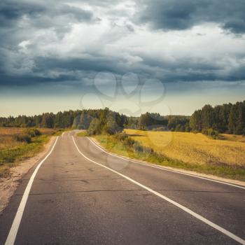 Empty turning rural highway under stormy cloudy sky, square European road landscape