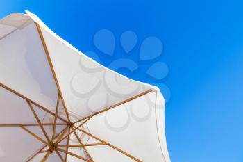 White outdoor umbrella under bright blue sky in summer day, resort background photo 