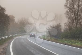 Rural foggy road background photo, car goes on empty highway in dark autumn foggy morning, stylized photo with warm tonal correction effect, old instagram style filter 