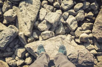 Male feet in blue canvas sport shoes standing on coastal rough rocky ground. Travel lifstyle background. Vintage warm tonal correction photo filter, old style effect