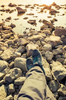 Male feet in blue canvas sport shoes standing on coastal rough rocky ground. Vertical travel lifstyle background. Vintage warm tonal correction photo filter, old style effect