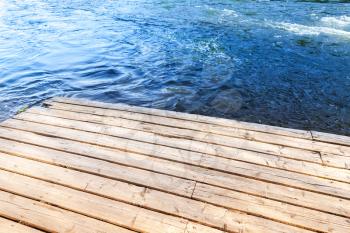 Corner of an old wooden pier with blue river water on a background