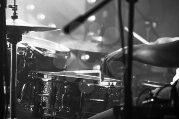 Black and white live music background, drummer plays with drumsticks on rock drum set. Closeup photo with soft selective focus