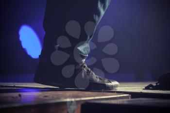 Feet of musican in black sneakers and jeans standing on the stage. Selective focus