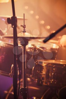 Live rock music background, drummer plays with drumsticks on rock drum set. Warm toned closeup vertcial photo, soft selective focus