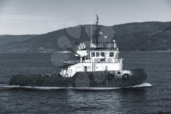 Tug boat with white superstructure underway, side view. Trondheim, Norway. Monochrome photo