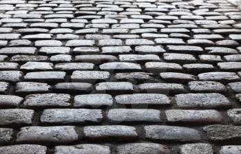 Dark shiny cobble road, stone street pavement background with selective focus