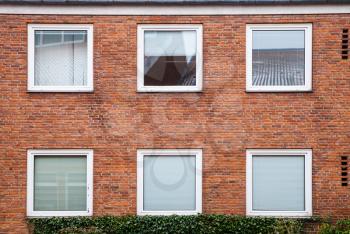 Red brick wall with square windows closed with white louvers, European living house facade, background texture