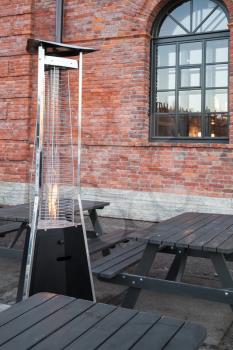 Outdoor gas heater stands near wooden tables on restaurant terrace 