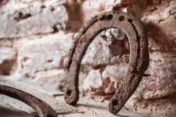 Old rusted horseshoe stands near brick wall, close up photo with selective focus