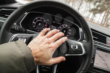 Driver hand pushes a steering wheel klaxon of luxury car. Closeup photo with selective focus