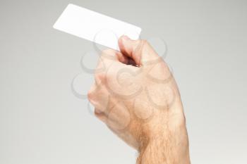 Male hand holds white card over gray background, close up photo, selective focus