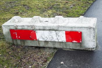 Concrete road block with red white striped warning sign lays on the roadside