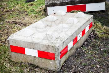 Concrete road blocks with red white striped warning signs lay on green grass