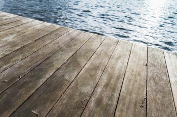 Edge of old wooden pier and blue rippled water, background photo