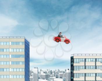 Young businessman driving car jumping between two high buildings
