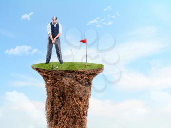 Businessman playing golf on the top of a grass cliff