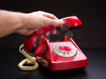 Hand picking up handset of red telephone