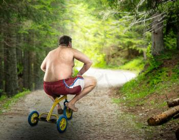 Adult naked man cycling in the forest on child's bicycle