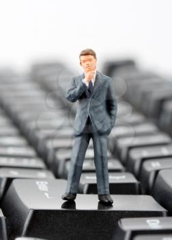 Miniature figurine of successful businessman standing on computer keyboard