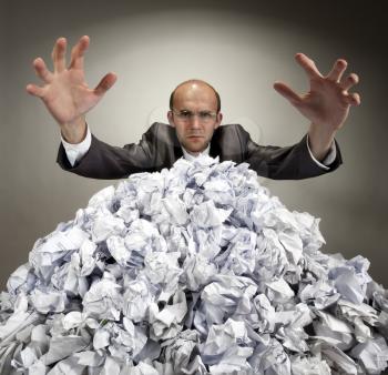 Serious businessman with raised hands reaches out from big heap of crumpled papers