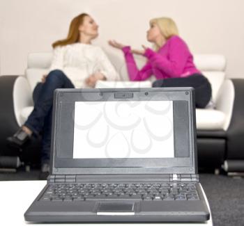 Laptop with blank screen and two talking woman on background