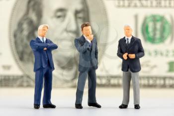 Miniature figurines of successful business team with $100 banknote on background