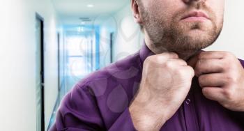 Bearded man buttons his shirt in office corridor