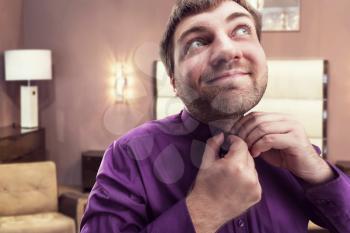 Bearded man buttoning his shirt at home interior