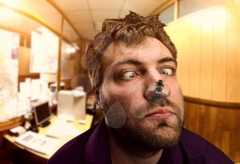Strange exhausted businessman looking at the fly on his nose in the office