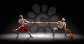 Two men fighting for sausages over black background