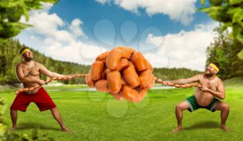 Two men fighting for a pile of sausages in the meadow