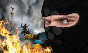 Serious man in a balaclava mask against burning Ukrainian Maidan