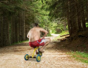 Adult strange man cycling in the forest on child's bicycle