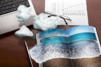 Office table in clouds with the sea on the notebook. Vacation concept