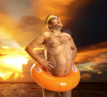 Strange naked man with children's buoy on an evening beach