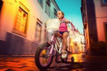 Smiling little girl cycling on pink bike on the street at night