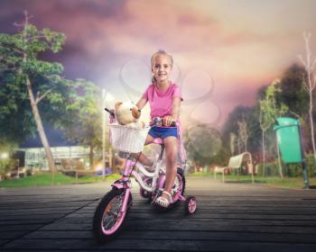 Smiling little girl cycling on pink bike on the street in the night