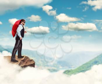 Businessman with red umbrella standing on the rock in the clouds