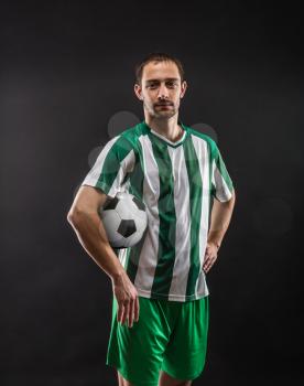 Confident football-player spinning soccer ball over black background
