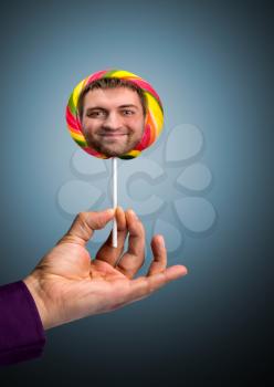 Male hand holding a lollipop with happy male face in it